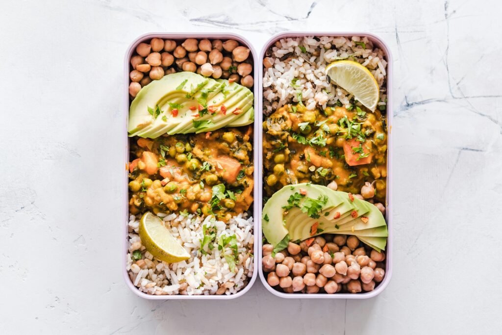 Delicious vegan lunchboxes featuring chickpeas, rice, avocado, and curry on a white background.